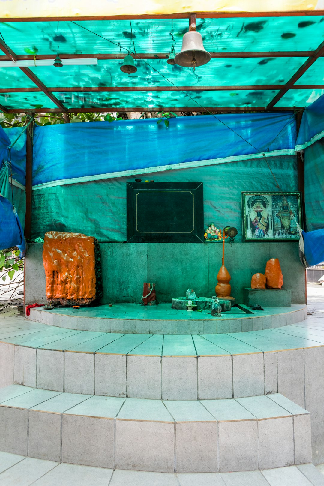 A small Hindu temple dedicated to Lord Shiva and Lord Hanuman on the streets of Mumbai, India by Aquarium Music a blue covered area with steps and a painting on the wall
